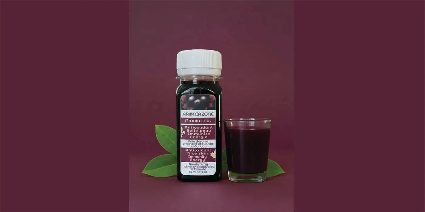 Une bouteille remplie d'un liquide violet foncé avec un bouchon blanc et une étiquette, arborant le nom de marque « arenizone » et la gamme de produits « oronia shot », est posée à côté d'un verre assorti.